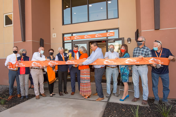 a group of people cutting a ribbon in front of the glass door of a building