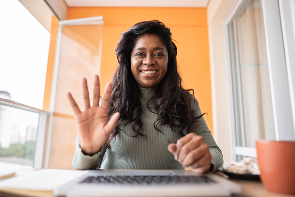 woman behind a desk facing forward and waving one hand