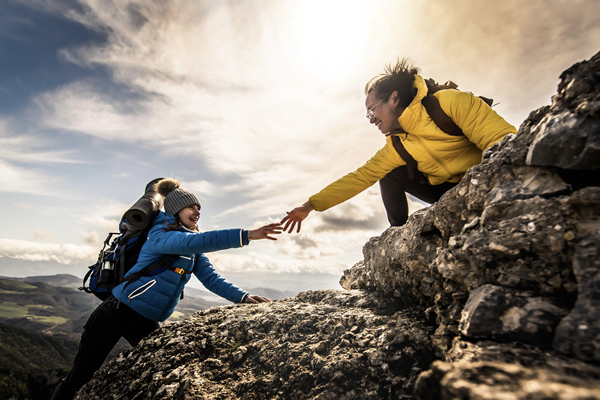 two people on a cliff, one reaching out to help the other